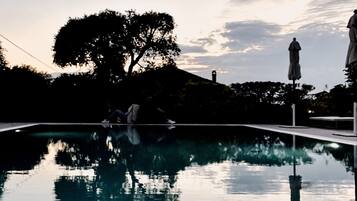 Una piscina con un reflejo claro, rodeada de árboles y una estatua.