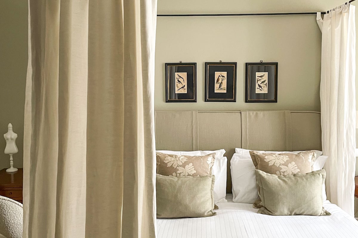 A bedroom with a canopy bed, a headboard with three framed pictures, and a bedside table with a lamp.
