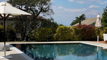 Piscina com superfície de água azul cristalina, rodeada por um espaço de deck com espreguiçadeiras e guarda-sóis.