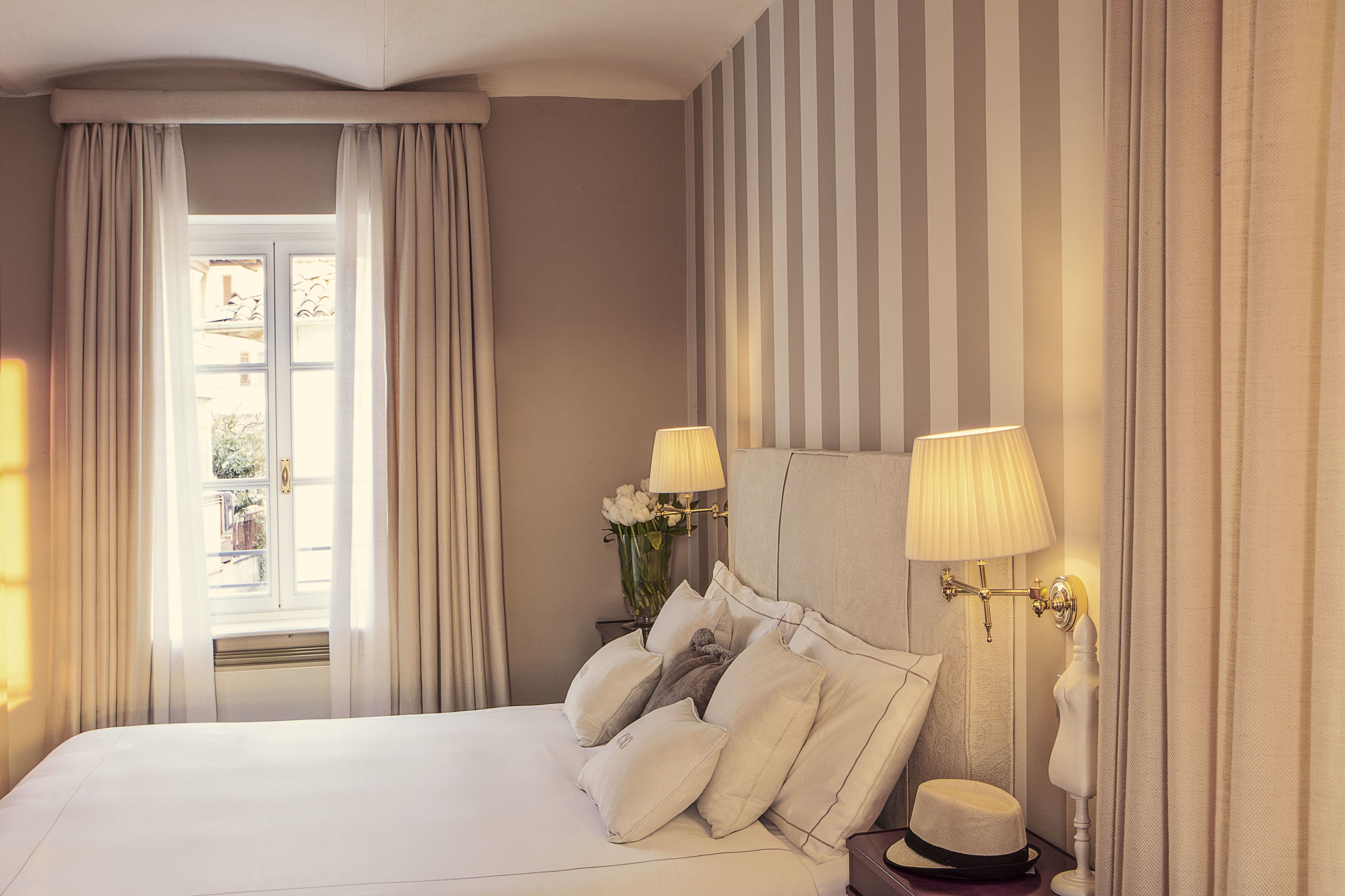 A neatly made bed with pillows, a bedside lamp, and a hat on a nightstand.