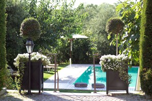 Un espace aménagé au bord de la piscine, avec une pergola, un lampadaire et une haie soigneusement taillée.