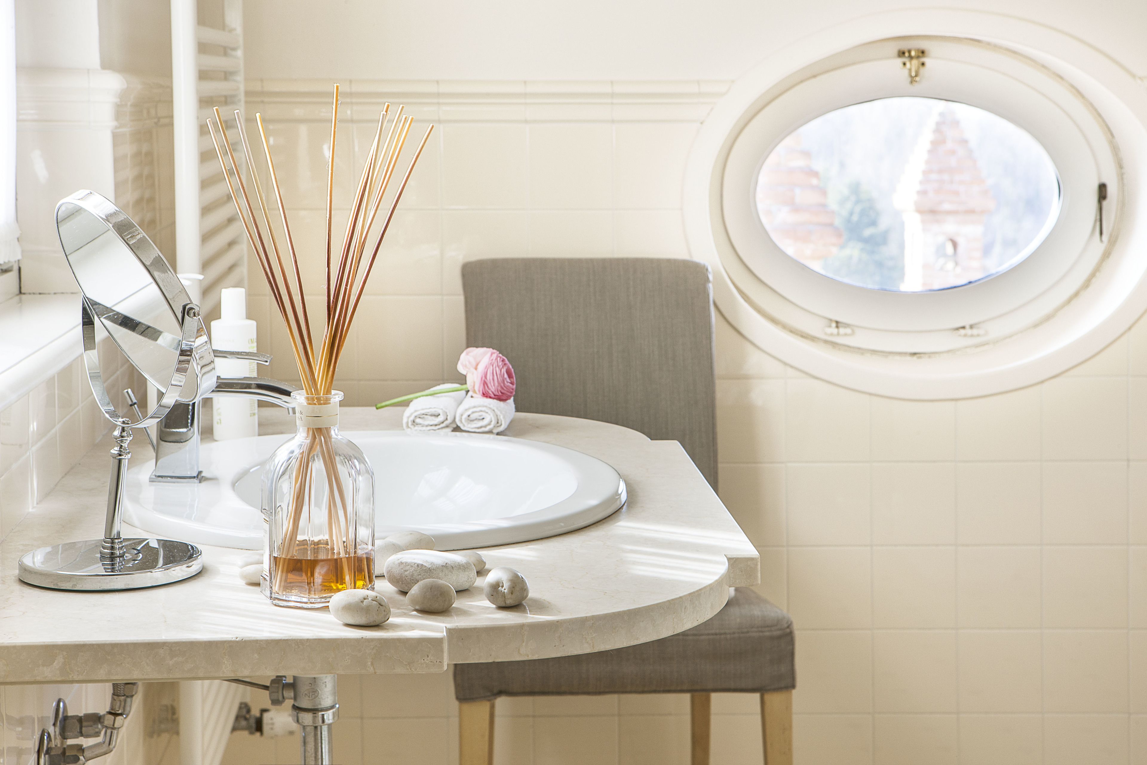 A bathroom with a round window, a mirror, a sink, and a towel.