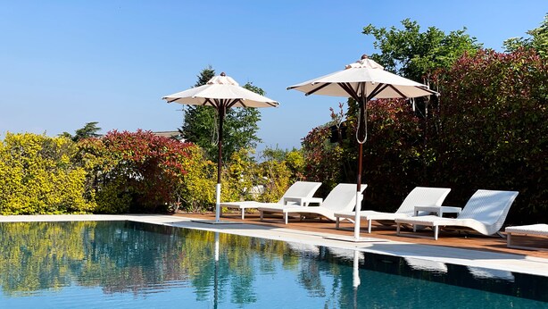 Un espace aménagé au bord de la piscine, avec des chaises longues blanches et des parasols, le tout entouré d’une végétation luxuriante.