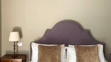 A neatly made bed with striped bedding, a headboard with a purple fabric and decorative bead trim, and a bedside table with a lamp and a power outlet.