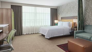 A hotel room with a bed, a desk, a TV, a sofa, and a window with curtains.