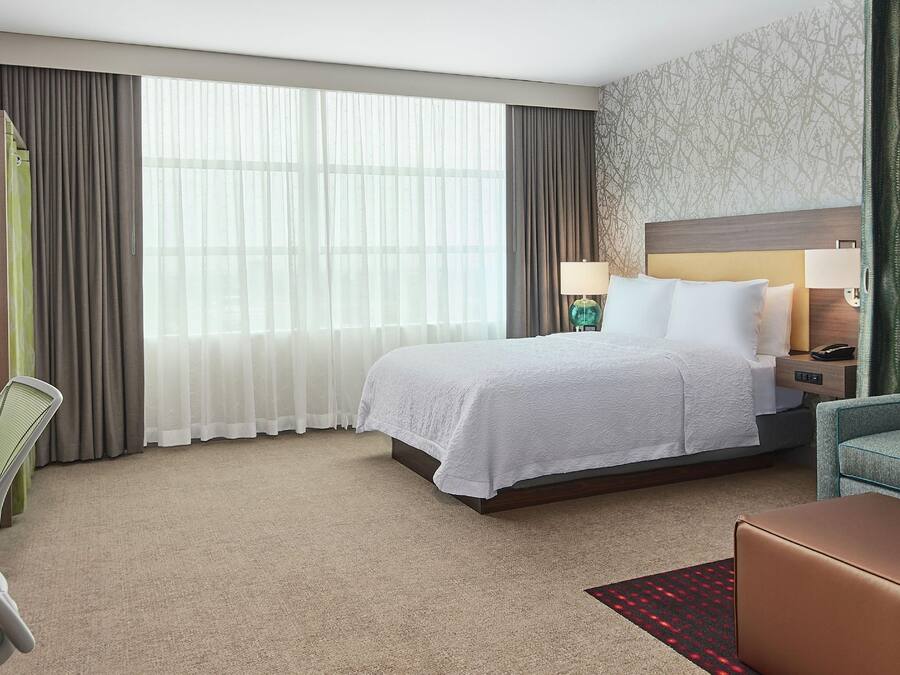 A hotel room with a bed, a desk, a TV, a sofa, and a window with curtains.