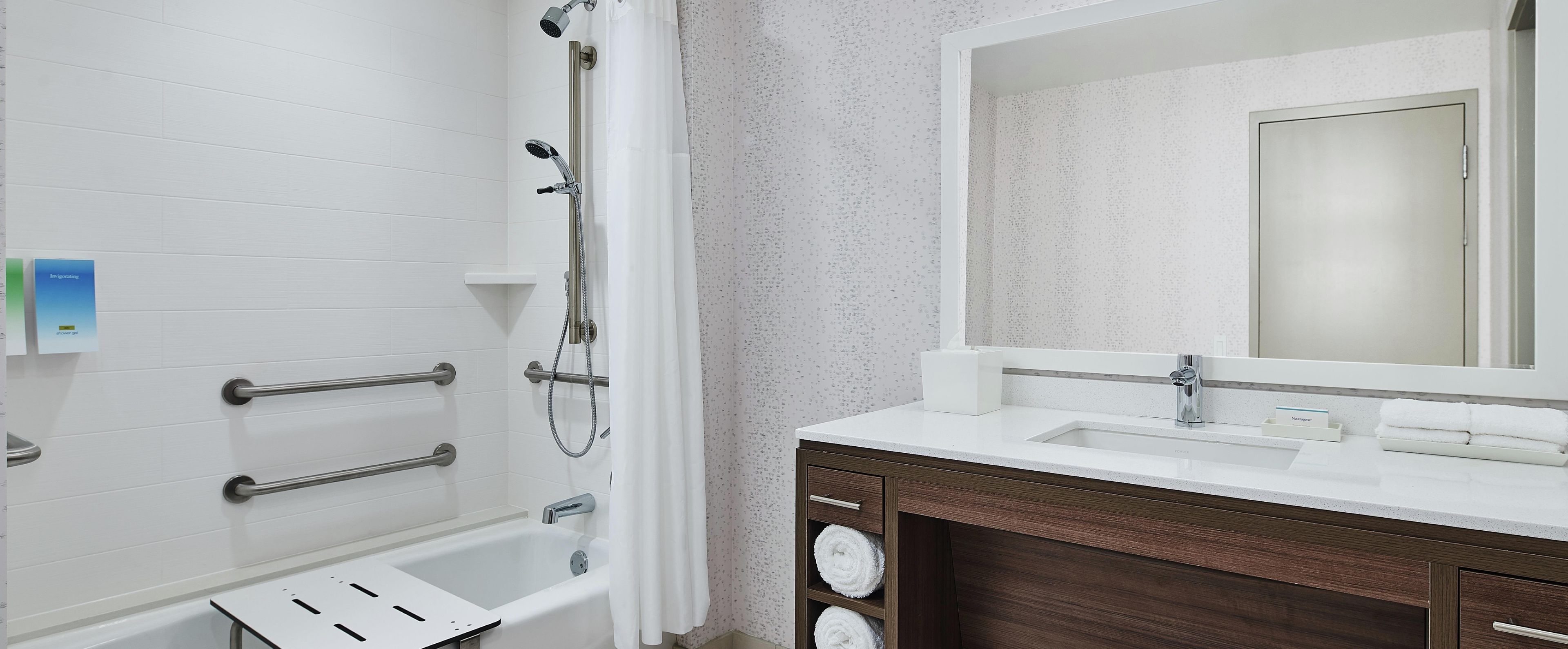 A bathroom with a shower, a sink, a mirror, and a towel rack.