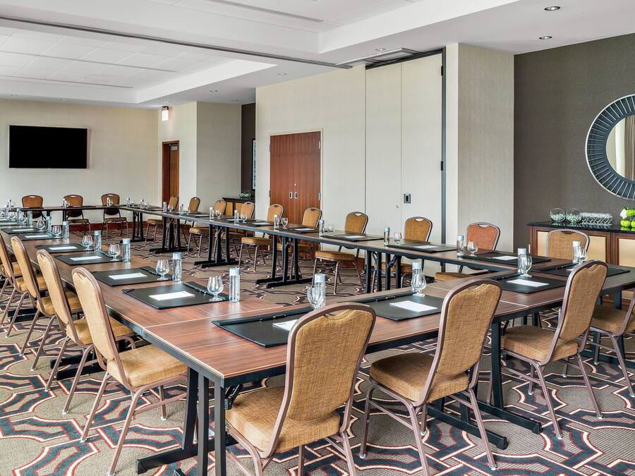 A conference room with long tables, chairs, and a large mirror on the wall.
