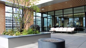 An outdoor seating area with a fire pit, a brick planter with greenery, and a modern building with large windows. - Home2 Suites by Hilton Chicago McCormick Place (Chicago)