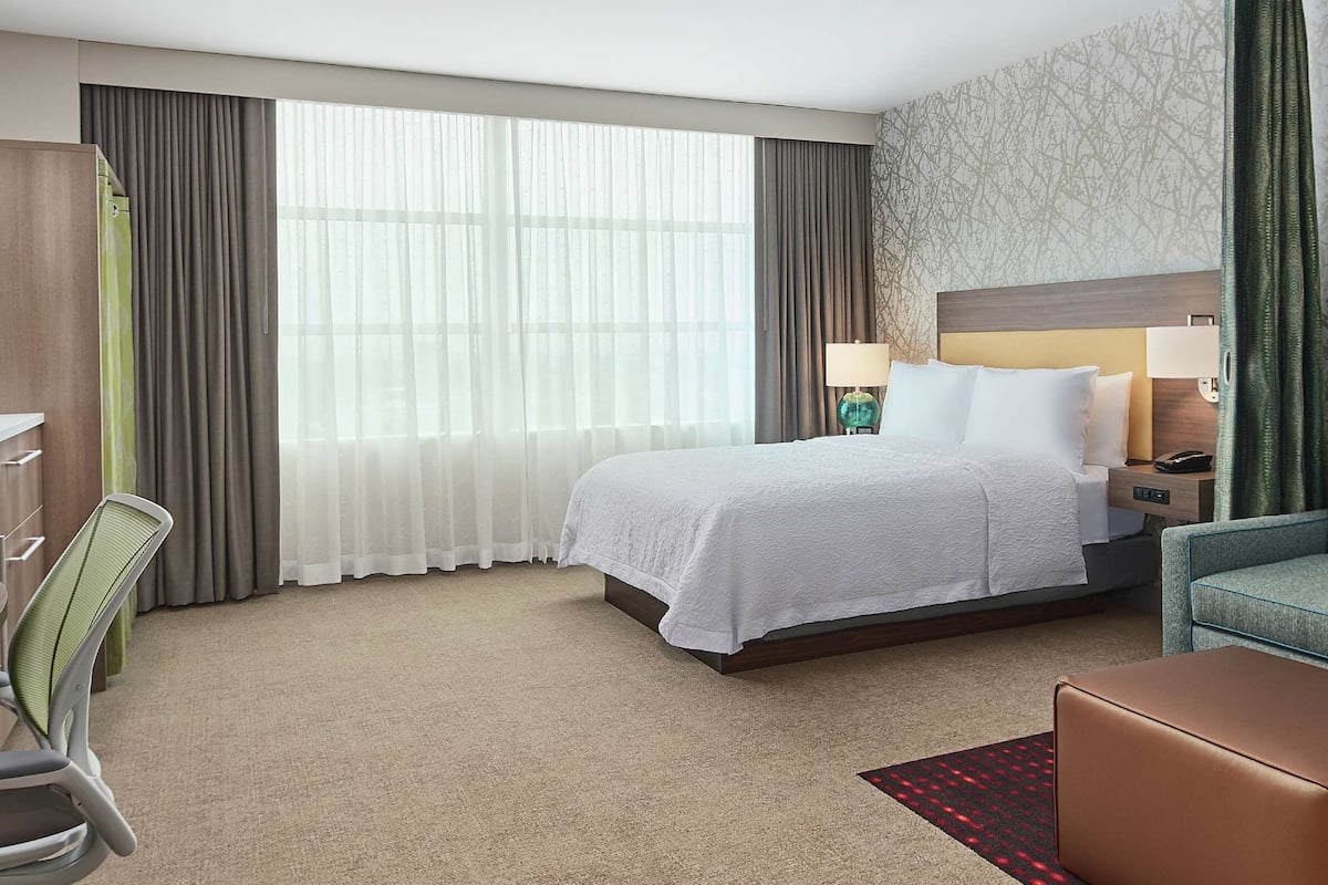 A hotel room with a bed, a desk, a television, a sofa, and a window with curtains.