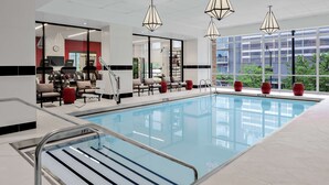 A modern indoor swimming pool with clear glass walls, a poolside seating area with chairs, and large windows offering views of the outside. - Home2 Suites by Hilton Chicago McCormick Place (Chicago)