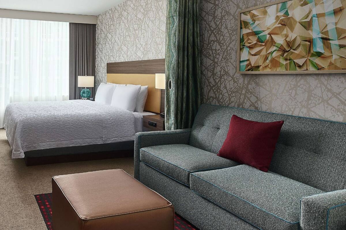 A hotel room with a bed, a sofa, a desk with a TV, and a chair.