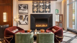 A modern living room with a fireplace, red sofas, green armchairs, and artwork on the walls. - Home2 Suites by Hilton Chicago McCormick Place (Chicago)