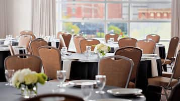 A dining area with tables set for service, chairs, and a view of buildings through large windows.