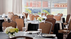 Un comedor con mesas dispuestas para el servicio, sillas y vistas de edificios a través de amplias ventanas.