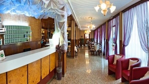 Un hall d’hôtel avec un comptoir d’accueil, un lustre et des fauteuils rouges.