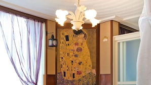Une pièce avec deux fauteuils rouges, un lustre, un grand tableau de Gustav Klimt et une vue sur la mer par une fenêtre.