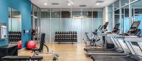 A gym with treadmills, weight machines, and a wall of dumbbells.