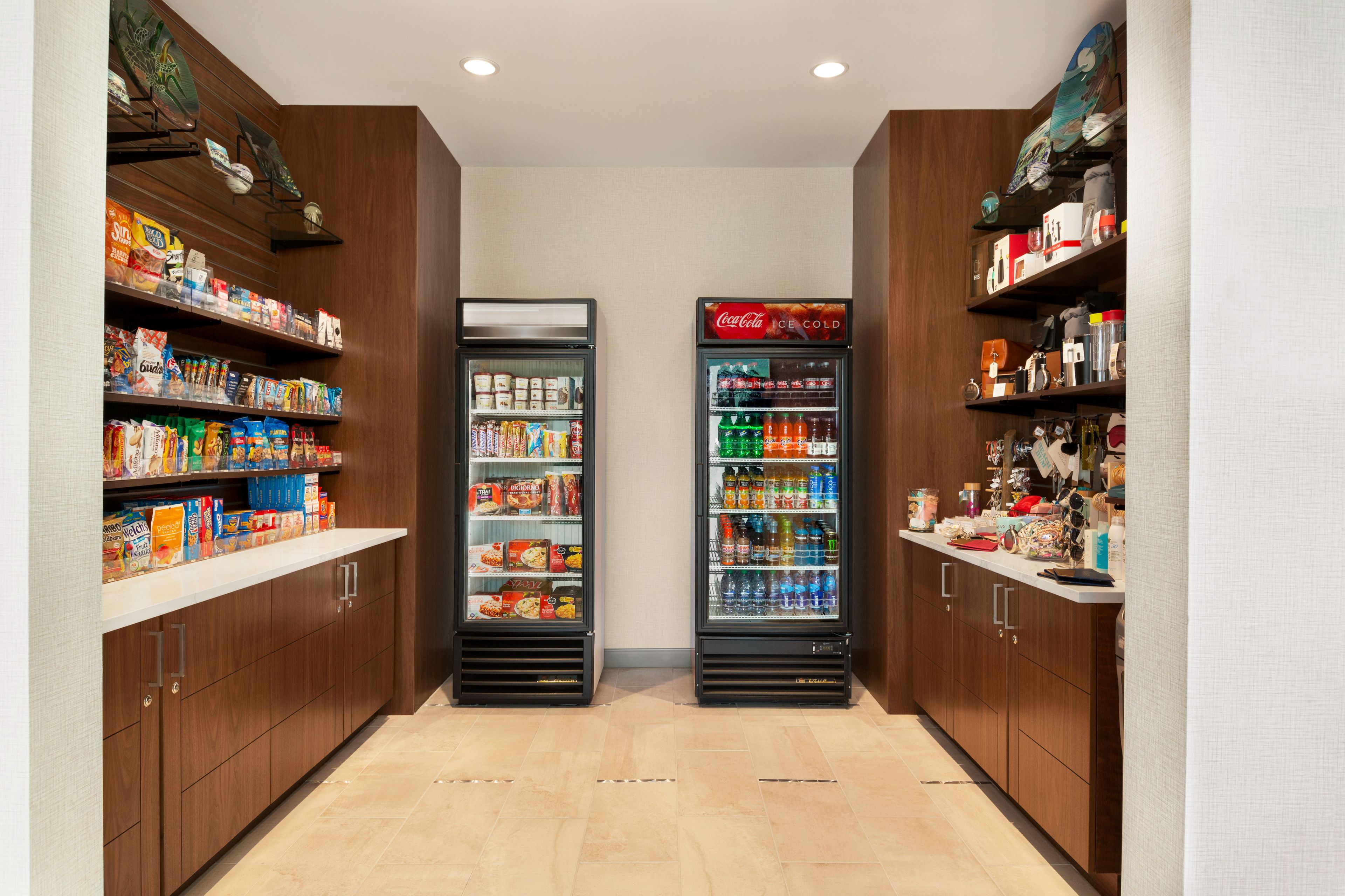 A narrow hallway with two refrigerated beverage dispensers and shelves stocked with snacks and beverages.