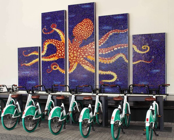 Una fila de bicicletas eléctricas con una obra de arte de pulpo en mosaico encima.