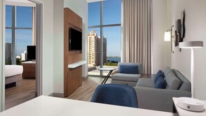 Une chambre d’hôtel moderne dotée d’une grande fenêtre, d’un téléviseur à écran plat, d’un canapé, d’une petite table et d’un bureau avec une lampe.