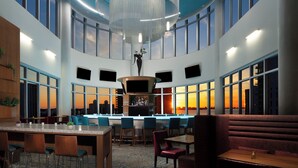 Un vaste espace intérieur comprenant un bar, des sièges et de grandes fenêtres offrant une vue sur le coucher du soleil.