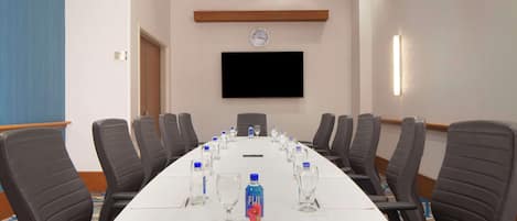 A conference room with a long table, chairs, water bottles, and a clock on the wall.