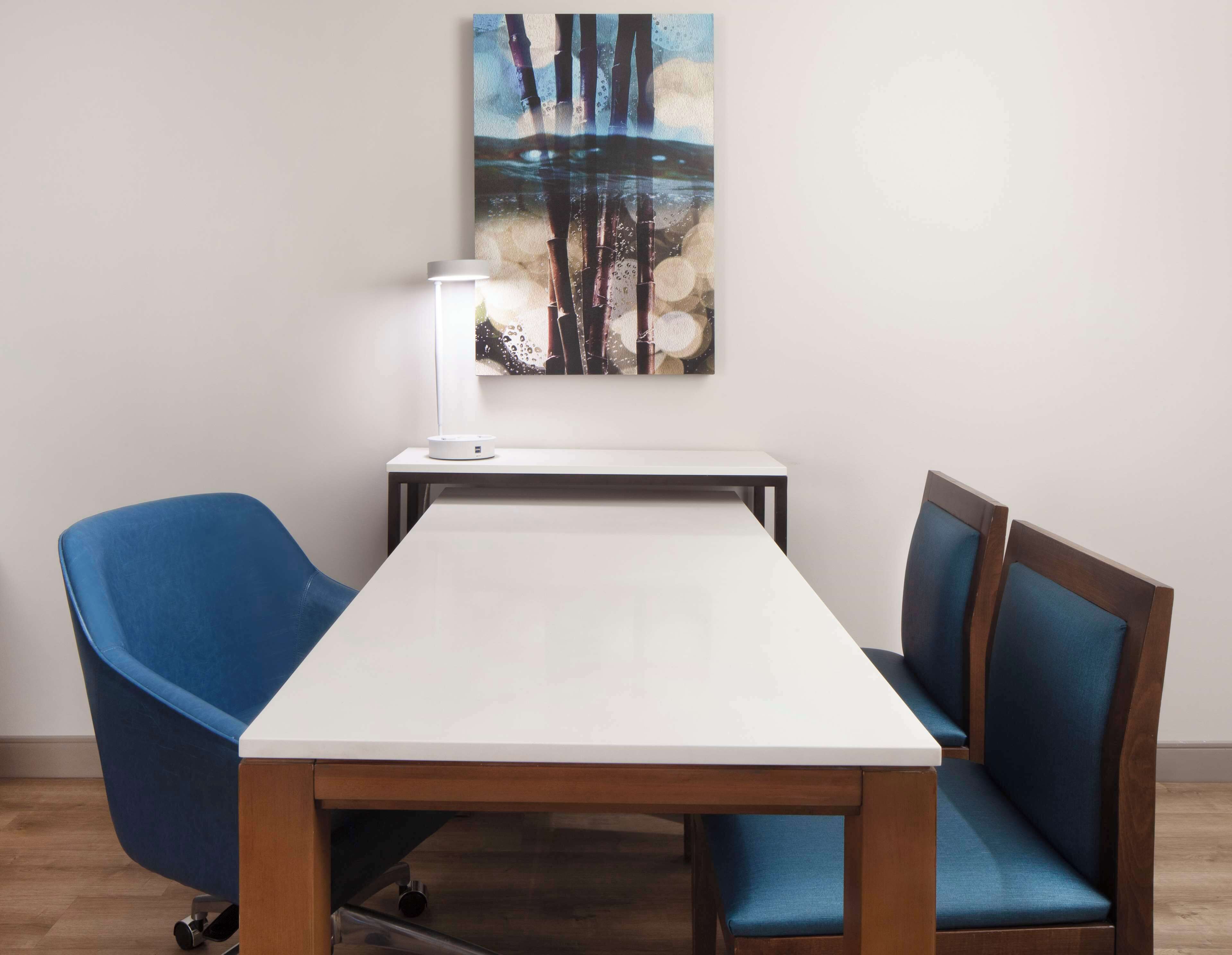 Une salle de conférence avec une table blanche, des chaises bleues, une lampe et un tableau accroché au mur.