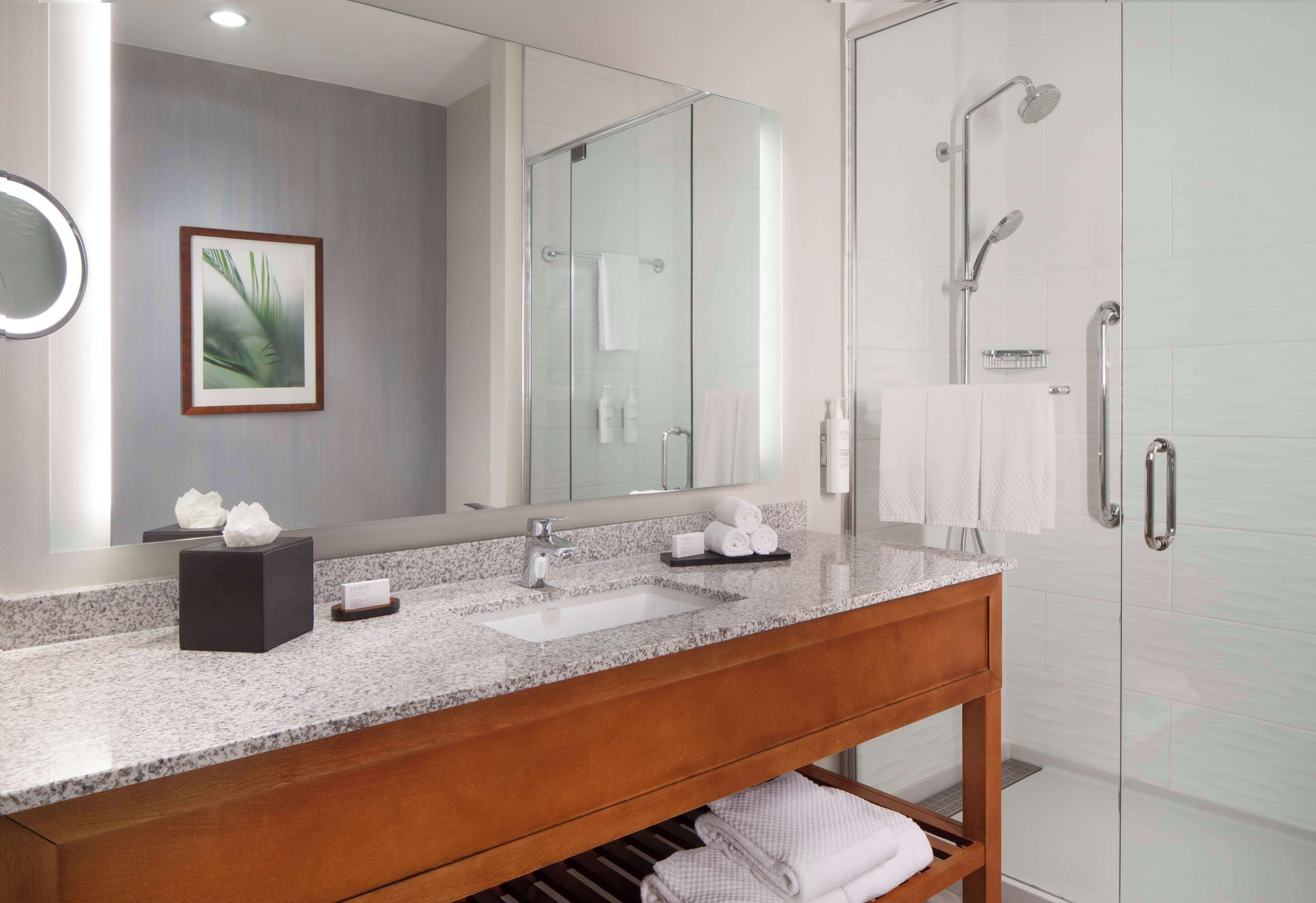 A modern bathroom with a granite countertop, a wooden vanity, a large mirror, and a glass-enclosed shower area.