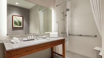 Un baño moderno con encimera de granito, tocador de madera, espejo grande, planta enmarcada, ducha con puerta de cristal y barra para toallas.