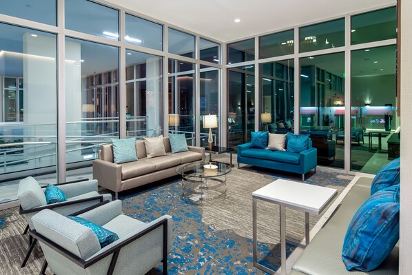 A spacious lobby with large windows, a beige sofa, a blue sofa, and a glass coffee table.