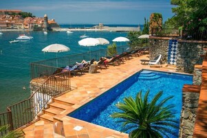 Un espace piscine avec vue sur la mer, des murs en pierre et des chaises longues.