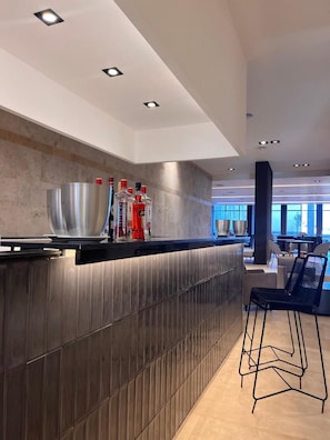 A modern bar area with a countertop, stools, and a view of the dining area.