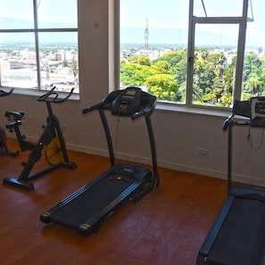 Un gimnasio con equipo de ejercicio y amplios ventanales con vistas a la ciudad.