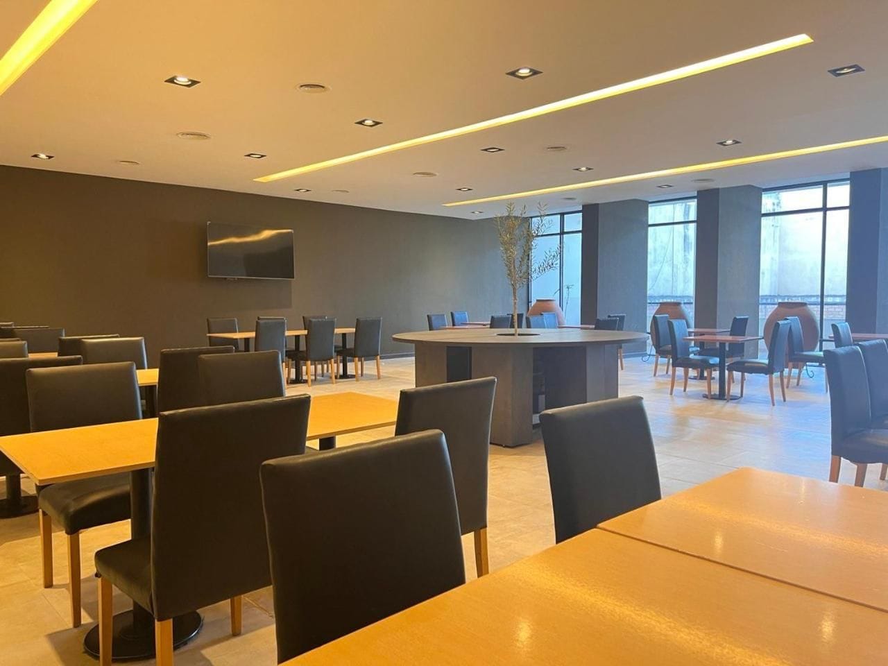Un espace repas moderne avec des tables et des chaises, un comptoir central et un téléviseur à écran plat fixé au mur.