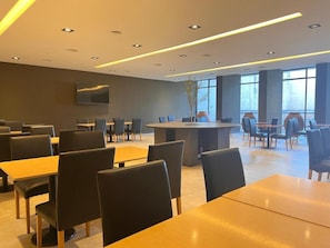 Un comedor moderno con mesas y sillas, una barra central y un televisor de pantalla plana montado en la pared.