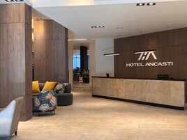 Zona de recepción de un hotel, con mostrador de recepción, un sofá con cojines y una pared de madera con el nombre del hotel.