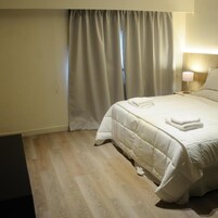 Habitación de hotel con cama, cortinas, lámpara de noche y suelo de madera.