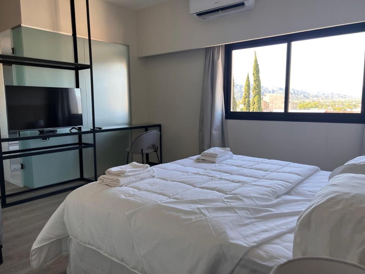 A hotel room with a bed, a desk with a chair, a television, and a window with a view of trees.
