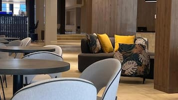 A modern interior with round tables and chairs, a sofa with patterned cushions, and a wooden accent wall.