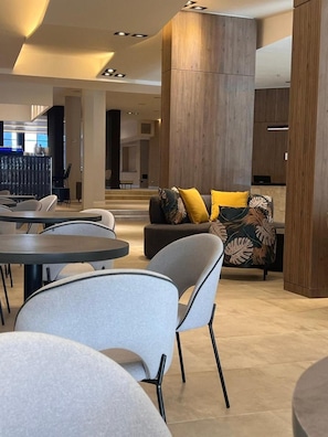 A modern interior with round tables and chairs, a sofa with patterned cushions, and a wooden accent wall.