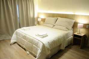 Una cama bien tendida con sábanas blancas y dos lámparas de noche, un cabecero de madera y una mesita de noche con lámpara.