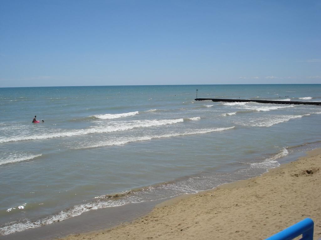 Een strand met een steiger die zich uitstrekt over rustig water, een zandstrand en een heldere lucht.