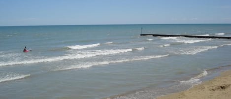A beach with a pier extending into calm waters, a sandy shore, and a clear sky.