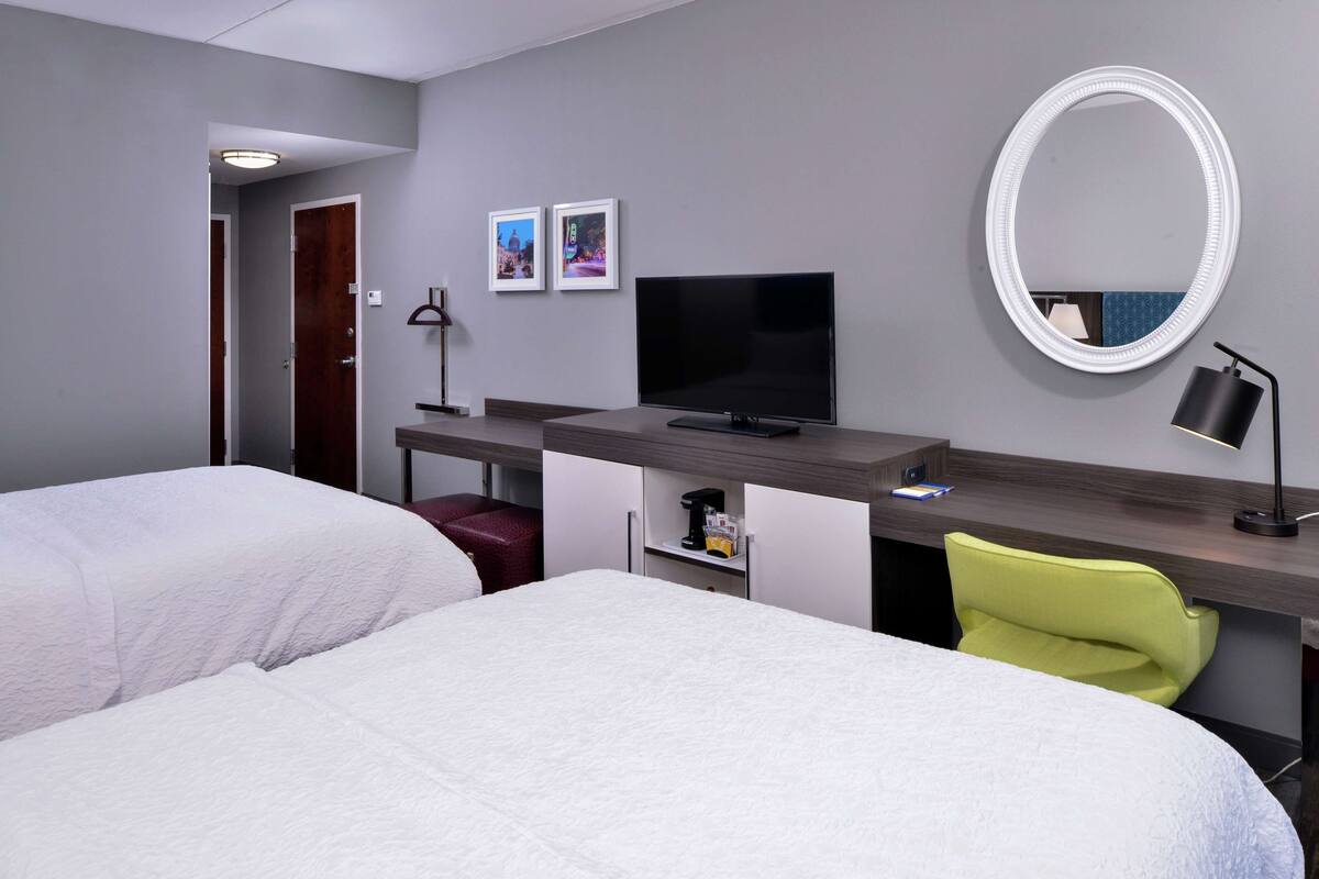 A hotel room with two beds, a desk with a TV, a mirror, and a chair.