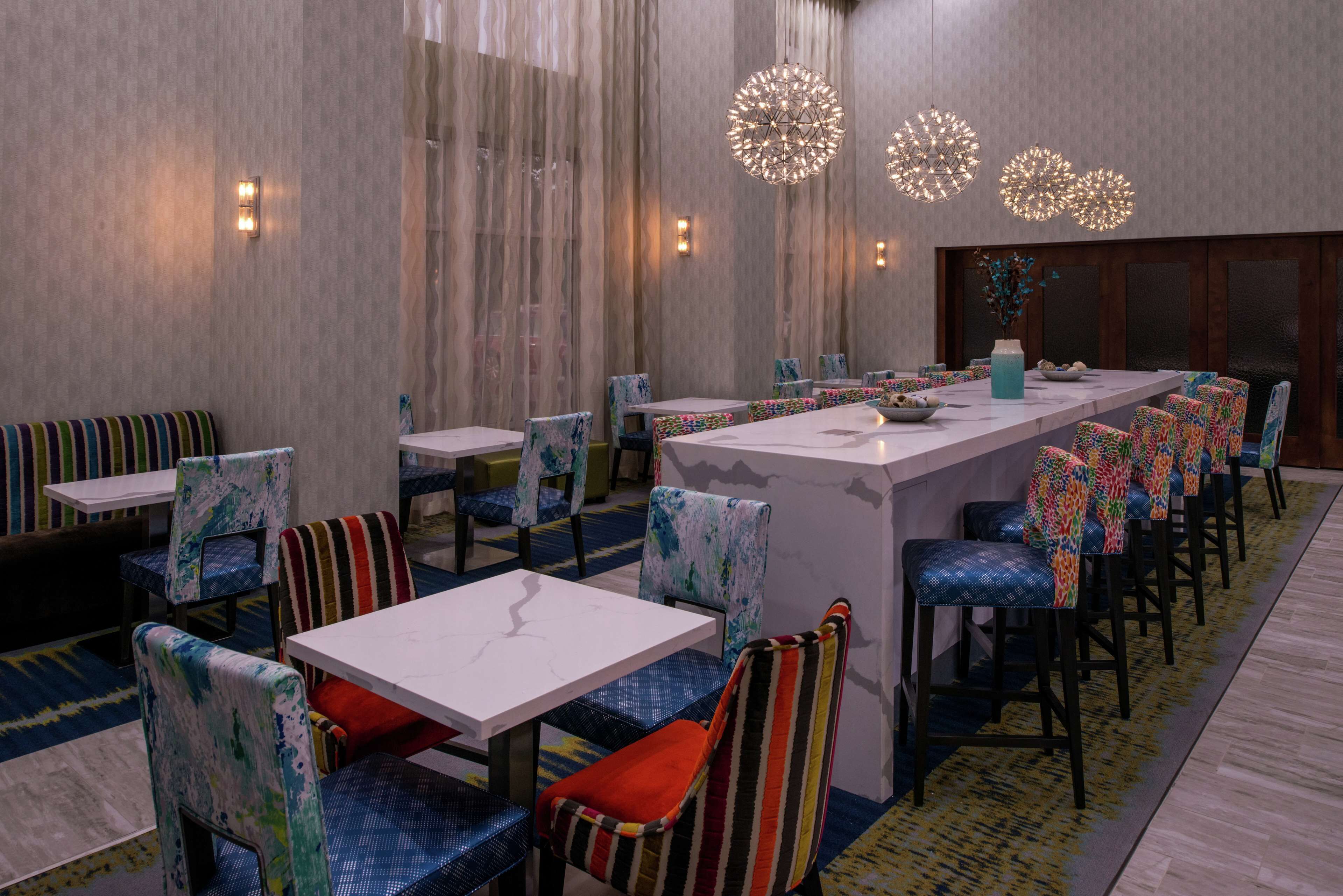 Un restaurante con una barra larga, sillas coloridas y luminarias modernas.
