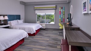 Ein Hotelzimmer mit zwei Betten, einem Schreibtisch, einem Stuhl und einem Fenster mit Blick auf Grünflächen.