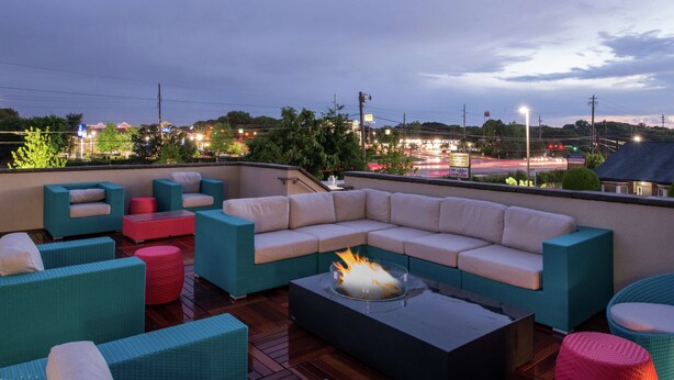 Eine Dachterrasse mit einer Eckcouch, mehreren Stühlen und einer Feuerstelle.