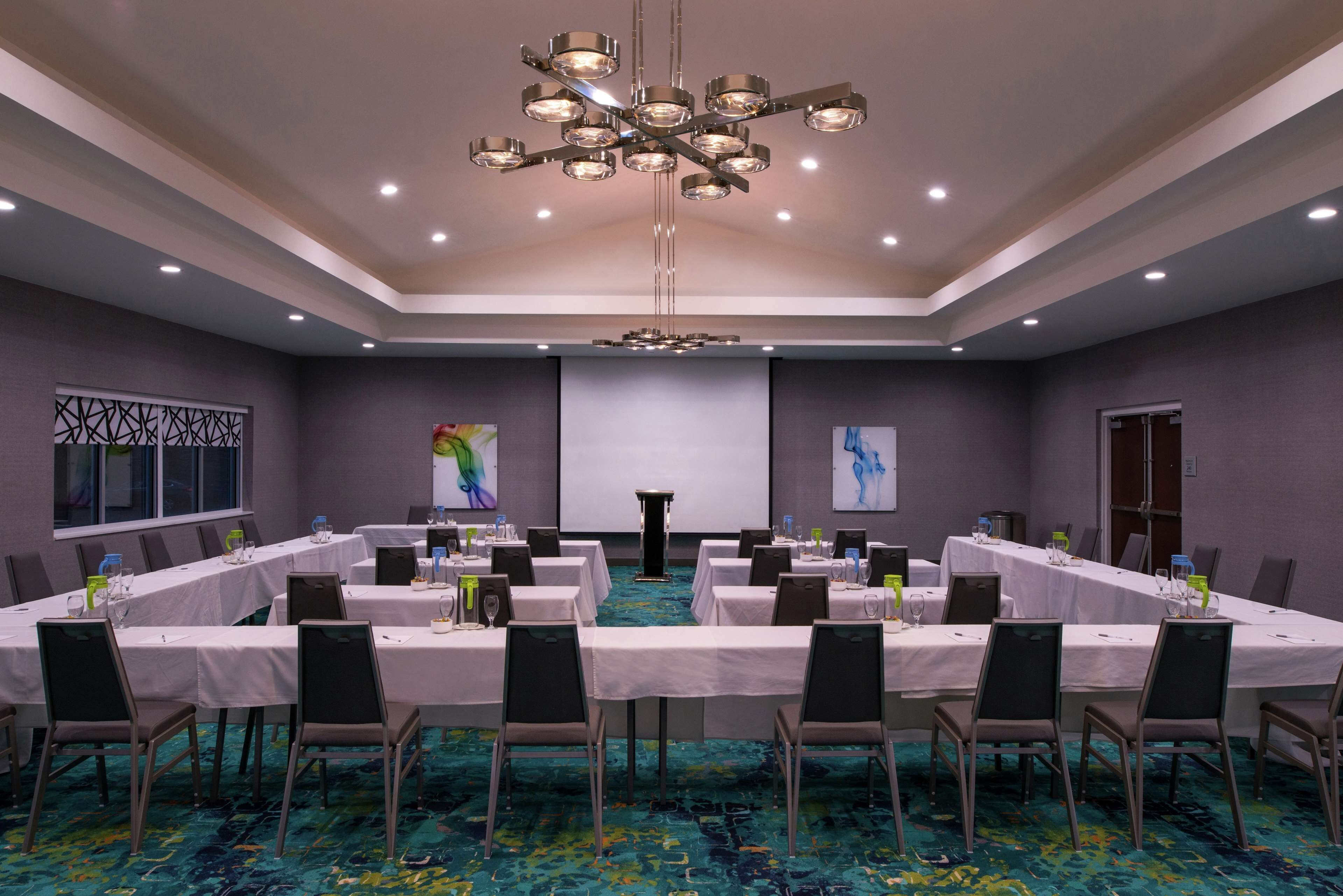 Une salle de conférence équipée de plusieurs tables, de chaises et d’un grand lustre.