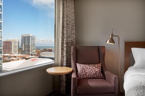 A hotel room with a city view, a round table, a patterned armchair, a floor lamp, and a bed with white linens. - Hilton Garden Inn Chicago McCormick Place (Chicago)